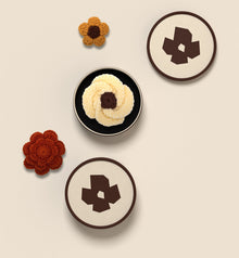Deux écrins LEZARE vus de dessus, l’un ouvert sur une fleur en crochet, fleurs posées autour